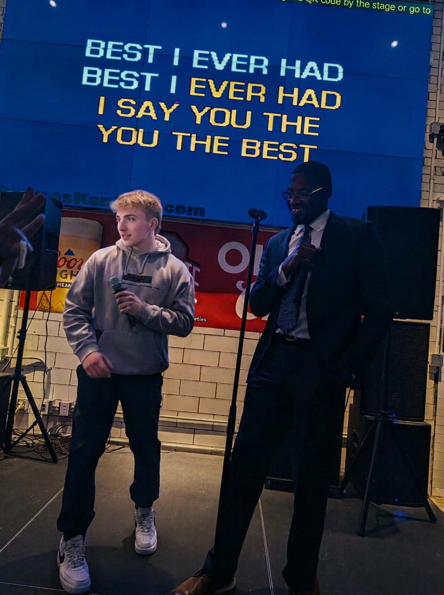 Two teammates sharing a microphone on a karaoke stage